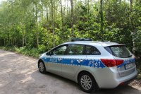 Radiowóz policyjny zaparkowany na drodze gruntowej przy lesie