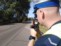 Policjant  Wydziału Ruchu Drogowego dokonuje pomiaru prędkości, trzyma w ręku miernik prędkości.