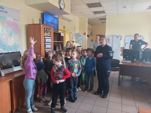 Dzieci z opiekunkami i policjantką, w pomieszczeniu dyżurnego komendy.